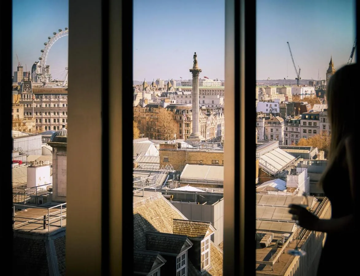 a woman looking out a window at a city at The Londoner in London